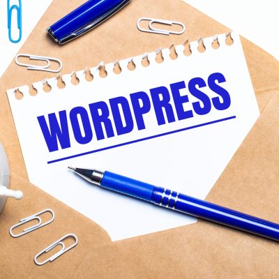 On a light background, a craft envelope, an alarm clock, paper clips, a blue pen and a sheet of paper with the text WORDPRESS.